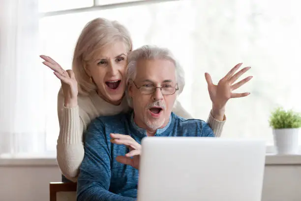 Photo of Excited senior couple looking at laptop surprised by good news
