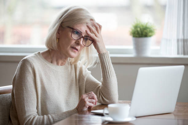 mujer madura confundida pensando en línea problema mirando portátil - recordatorio fotografías e imágenes de stock