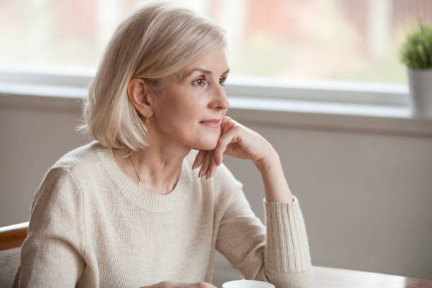 Thoughtful middle aged beautiful woman looking away drinking coffee