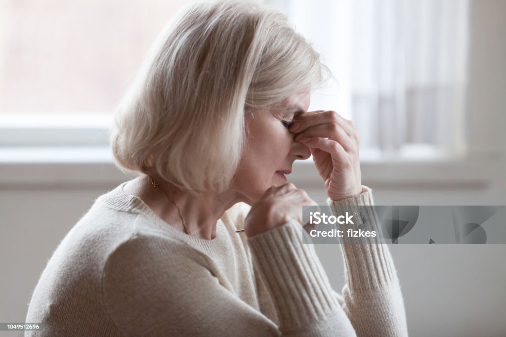 Fatigued upset older woman massaging nose bridge feeling eye strain Fatigued upset middle aged older woman massaging nose bridge feeling eye strain or headache trying to relieve pain, sad senior mature lady exhausted depressed weary dizzy tired thinking of problems Reminder Stock Photo