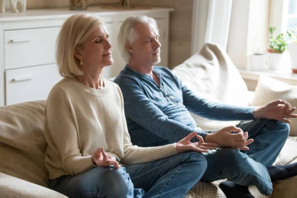istock Senior couple meditating practicing yoga together sitting at home sofa 1049512784