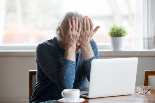 Fatigued senior man feeling tired from computer rubbing irritated eyes