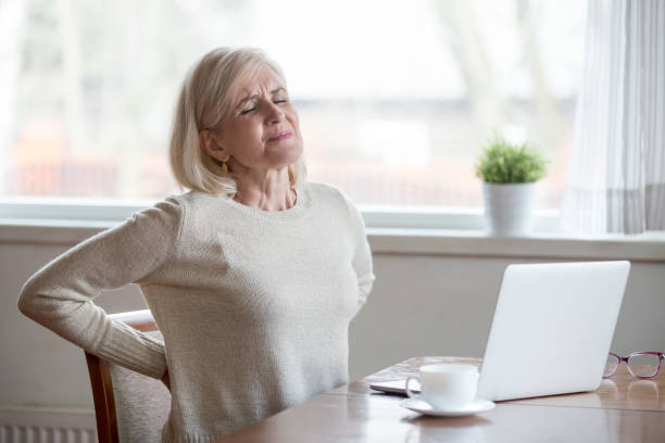 verärgert reife frau sitzen gefühl rückenschmerzen schmerzende muskeln massieren - backache pain women illness stock-fotos und bilder