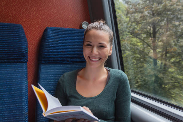 istock young cute woman smiling and reading a book while travelling by train 1049516958