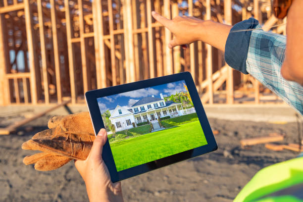 istock Female Construction Worker Reviewing House Photo on Computer Pad at Construction Site 1049517112