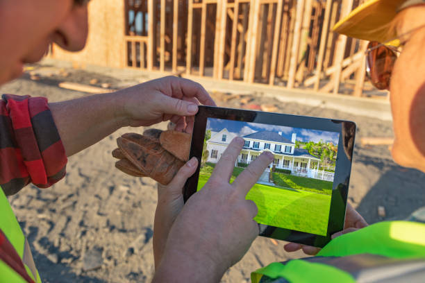 istock Male and Female Construction Workers Reviewing House on Computer Pad at Construction Site 1049519932