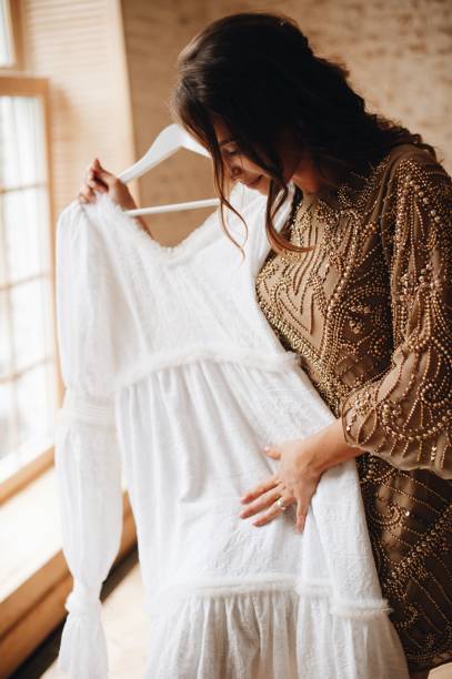 istock Woman Holding Wedding Dress While Standing Against Wall 1049534544