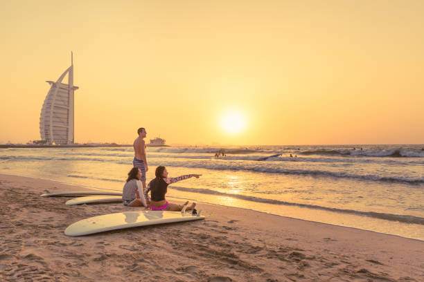 Dubai,UAE - October 04 2017:  Three Surfers go into the beach to catch a wave at a public beach in Dubai, UAE around sunset. Beautiful Golden hour light with a 7 star luxury hotel in backdrop.