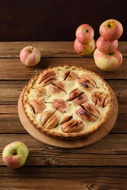 Tasty apple tart with cream filling served with raw organic apples on old wooden background copyspace