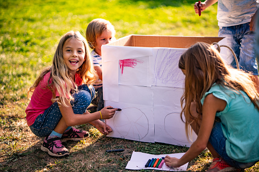 Children coloring cardboard box in park