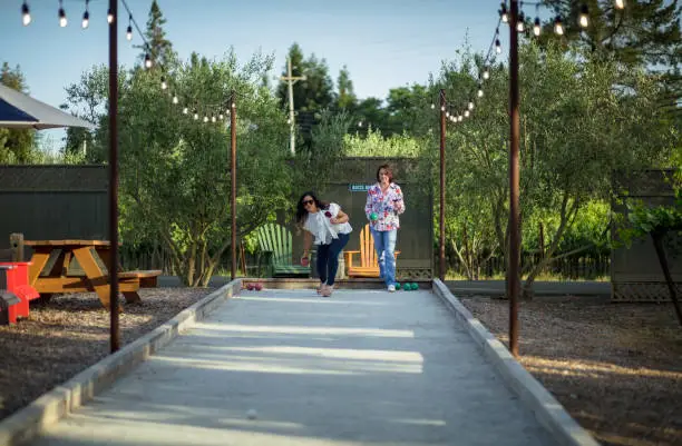 Two middle aged women playing bocce ball on a sunny afternoon.