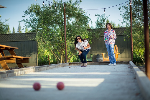 Two middle aged women playing bocce ball on a sunny afternoon.