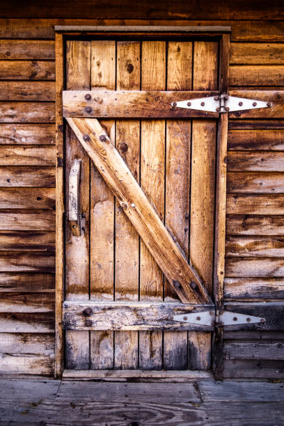 An old wooden door, leading to a wood building or a barn, with wooden handle. The building has been weathered for many years and shows significant water damage low on the walls.