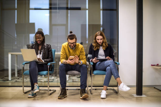 Young people using technology in waiting room Students relaxing between lessons, using different devices to surf the internet in waiting room, at University exclusion group of people separation fish out of water stock pictures, royalty-free photos & images