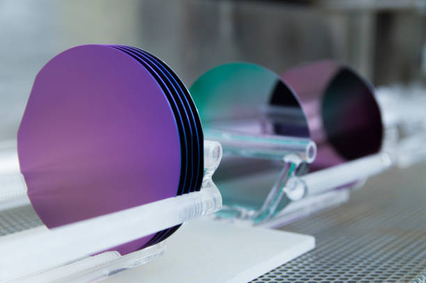 Vibrant Colors on Silicon Wafers This is a set of 100 mm silicon wafers grown in a cleanroom facility.  They are sitting in quartz holders or boats after being in a silicon dioxide growth furnace.  The high heat from the furnace combined with oxygen converts the surface of the wafers to silicon dioxide.  The wafer colors are dictated by the thickness of the silicon dioxide layer and the viewing angle.  The purples and greens shown on these wafers are quite common and give the cleanroom a colorful and artistic touch. cleanroom stock pictures, royalty-free photos & images