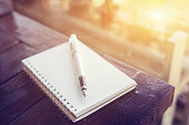 pen on the desk,Open a blank white notebook on wooden table and green bokeh background ,vintage color,selective focus