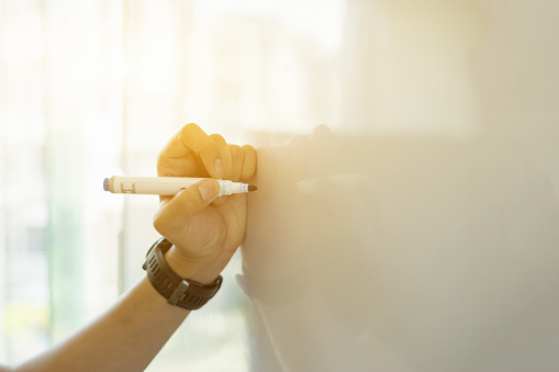 businessman putting his ideas on white board during a presentation in conference room. Focus in hands with marker pen writing in flipchart document notes,copy space