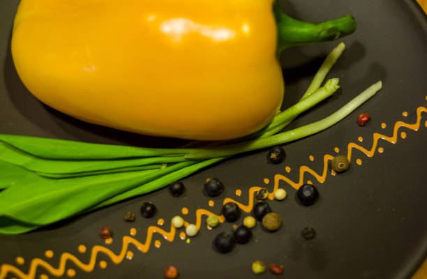 large yellow bell pepper and fresh green onions on a ceramic plate close-up