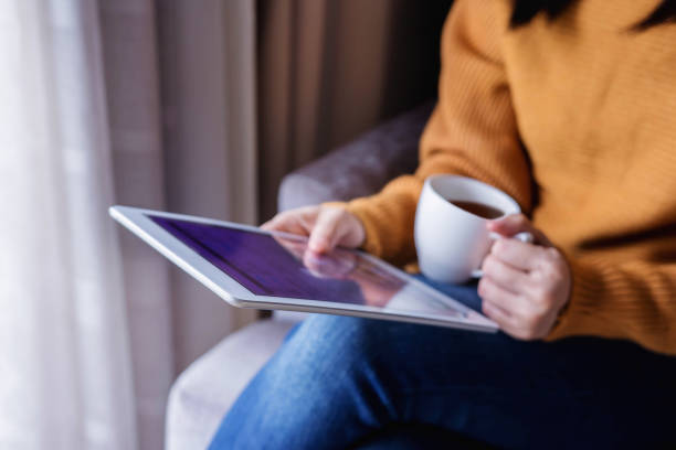 istock Reading Concept. Young Woman using Tablet and Drinking Coffee. Relaxing in Cozy House, Sit on the Chair, Front View and Selective Focus 1049661684