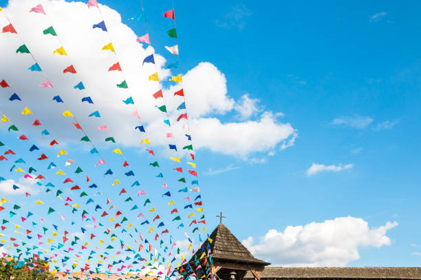Multi-colored flags against a blue sky with clouds and a dome of a church.