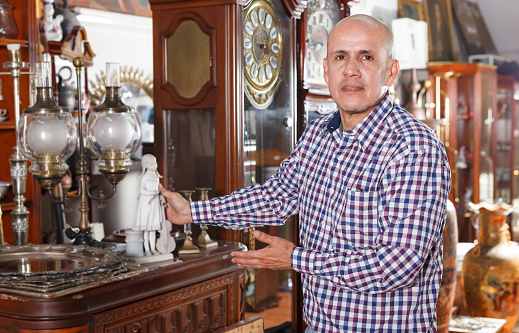 Portrait of adult man collector is showing of rare items in interior of antique store