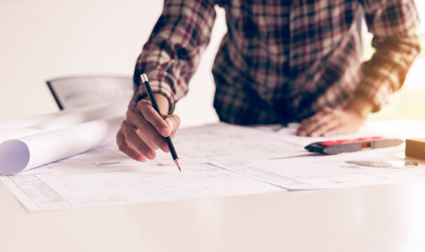 istock Hand of young engineering man drawing on blueprint. 1049701638