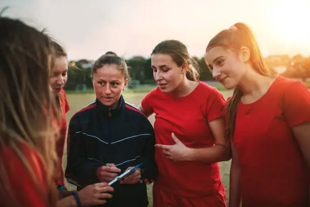 Women's soccer team talking with their female coach on training.