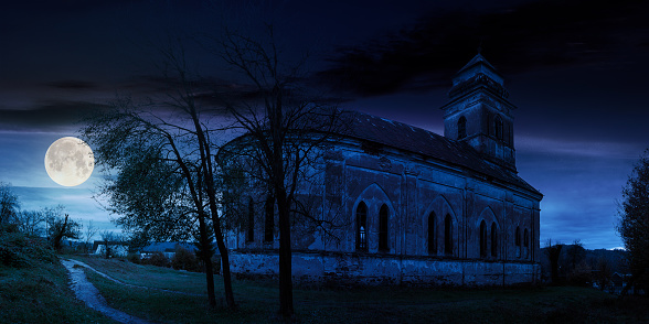 panorama of abandoned catholic church on hill at night in full moon light