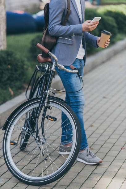 istock cropped view of man with coffee to go using smartphone and leaning on bicycle 1049719078
