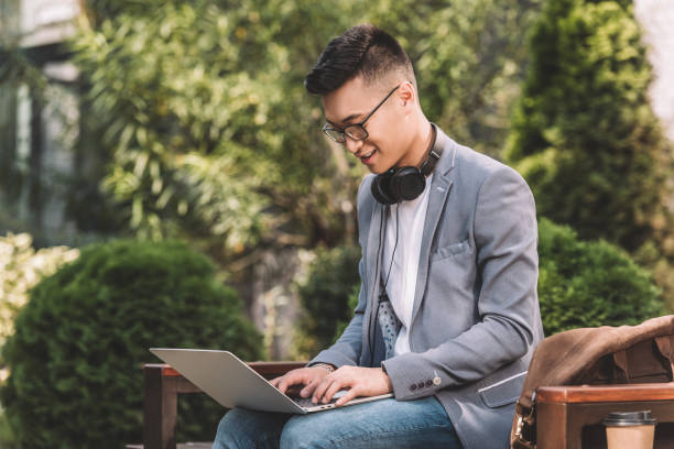 istock stylish asian freelancer in gray jacket working on laptop while sitting on bench 1049719262
