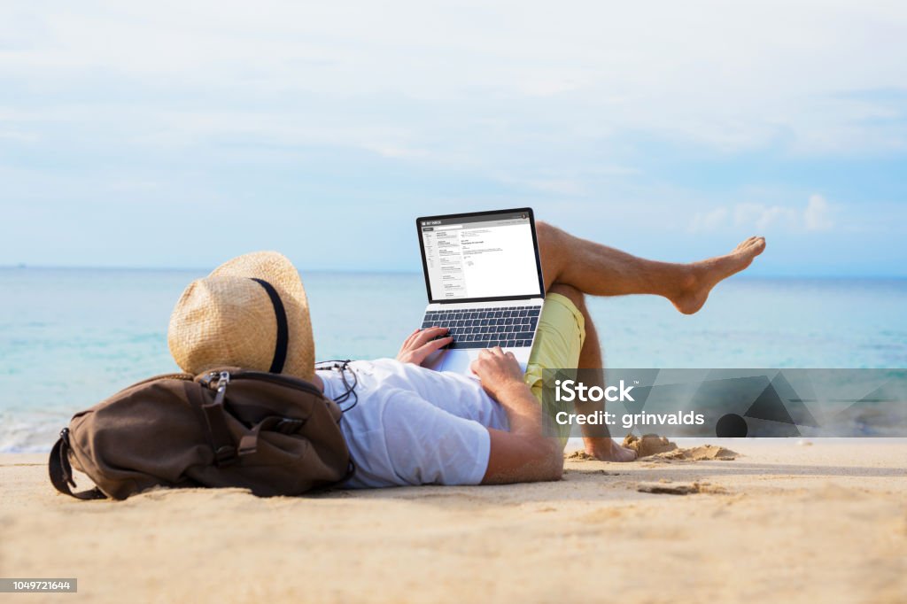 Mann liest e-Mails am Laptop beim Entspannen am Strand - Lizenzfrei Strand Stock-Foto