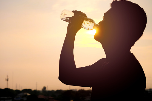 The silhouette of a man drinking a refreshing bottle of water on a sunset background