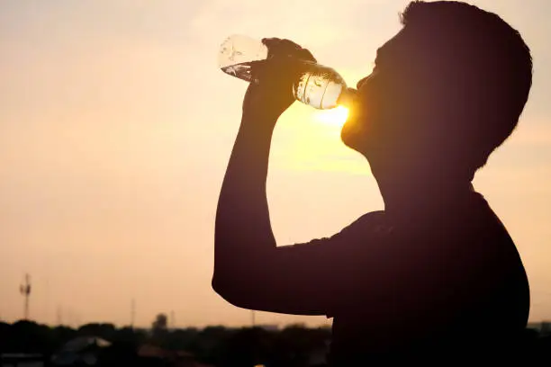 Photo of The silhouette of a man drinking a refreshing bottle of water on a sunset background
