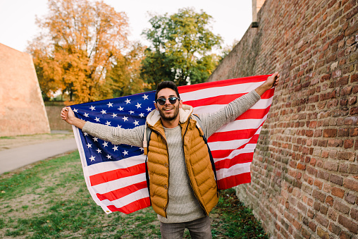 Handsome young man with sunglasses waving united states flag outdoors.