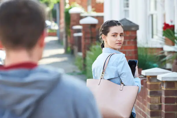 Photo of Young Woman Texting For Help On Mobile Phone Whilst Being Stalked On City Street