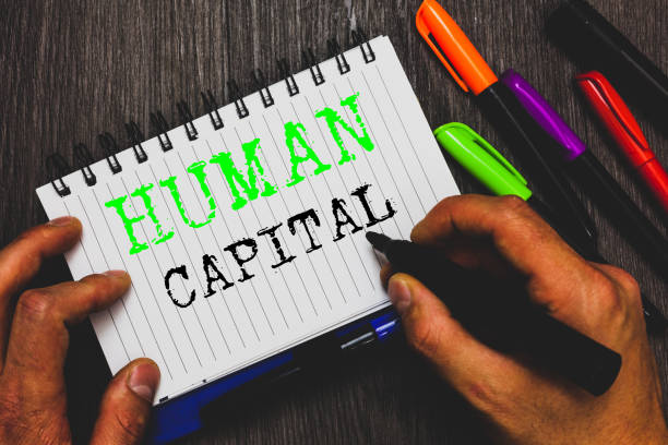 istock Handwriting text writing Human Capital. Concept meaning Intangible Collective Resources Competence Capital Education Man holding marker notebook paper communicating ideas Wooden background. 1049737386