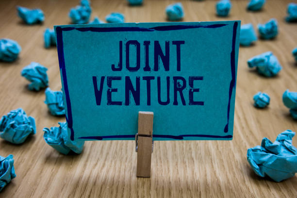 istock Handwriting text writing Joint Venture. Concept meaning Collaboration Arrangement Parties Partnership Team Clothespin holding blue paper note crumpled papers several tries mistakes. 1049737602