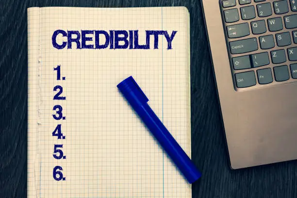 Photo of Text sign showing Credibility. Conceptual photo Quality of being convincing trusted credible and believed in Open notebook squared page black marker computer keyboard wooden background.