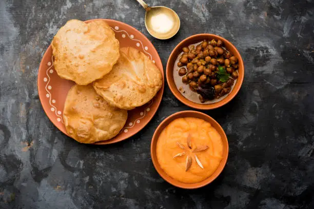 Photo of Suji/Sooji Halwa Puri or Shira Poori with black chana masala breakfast, served in a plate and bowl. selective focus