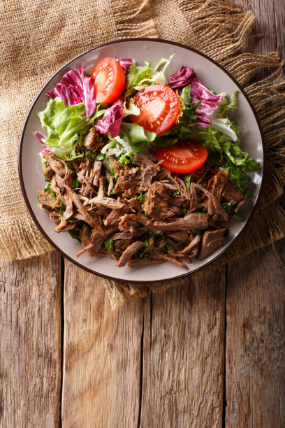 istock Delicious food: slow cooked pulled beef with fresh vegetable salad close-up. Vertical top view from above 1049743320