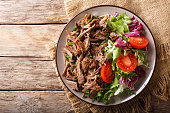 Delicious food: slow cooked pulled beef with fresh vegetable salad close-up. Horizontal top view from above