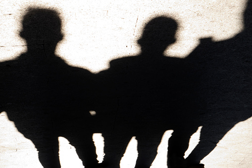 Blurry silhouettes and shadows of three man standing on city sidewalk in the night