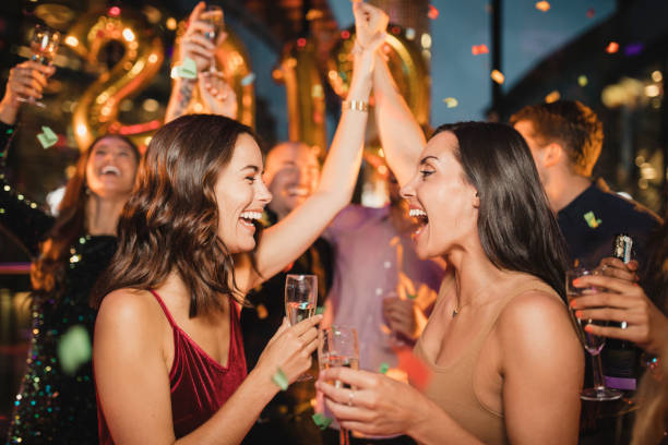 Celebrating the New Years Eve Count Down Two friends dancing among other people while celebrating the new year with a glass of champagne, balloons and confetti. new years 2019 stock pictures, royalty-free photos & images