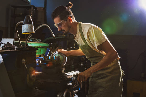istock concentrated male manufacture worker in protective apron and goggles using machine tool at factory 1049758234