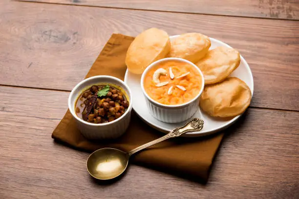 Photo of Suji/Sooji Halwa Puri or Shira Poori with black chana masala breakfast, served in a plate and bowl. selective focus