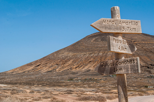 La Graciosa, Lanzarote, Canary Islands, Spain - September 12, 2018: Montana Pedro Barba, the twin-summitted and twin-cratered volcano of La Graciosa, the main archipelago island Chinijo, and the wooden signs to the main island attractions