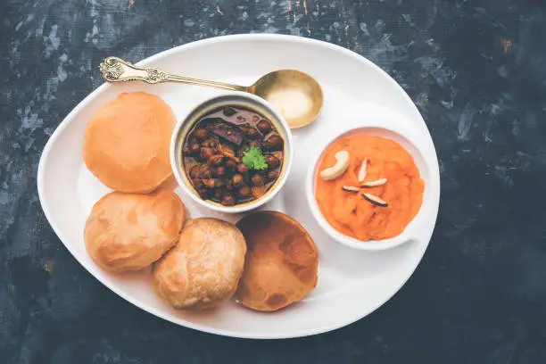 Suji/Sooji Halwa Puri or Shira Poori with black chana masala breakfast, served in a plate and bowl. selective focus