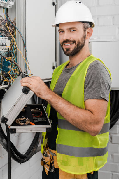istock smiling handsome electrician holding toolbox near electrical box in corridor and looking at camera 1049768822