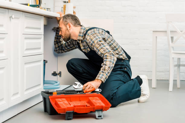 istock handsome plumber holding adjustable wrench and looking under broken sink in kitchen 1049768926