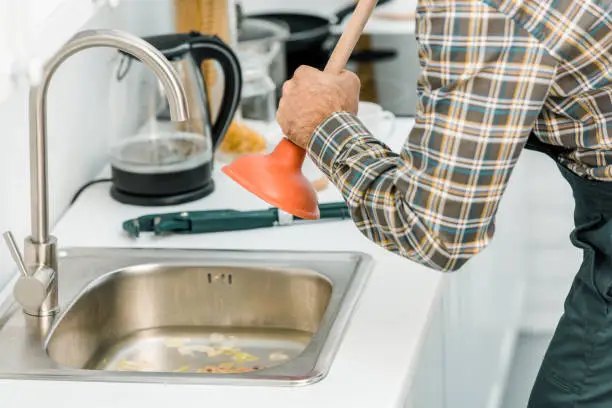 cropped image of plumber using plunger and cleaning sink in kitchen